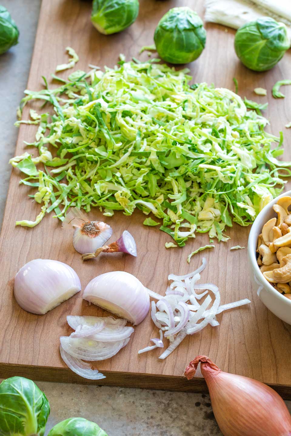 Partially sliced shallots on cutting board with a pile of shredded Brussel sprouts behind.