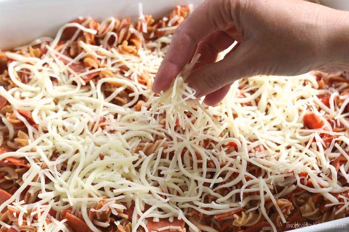 Hand sprinkling shredded mozzarella cheese on casserole before baking.