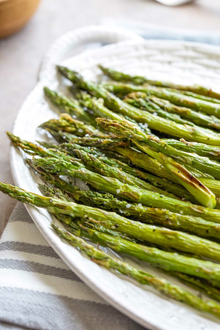 Finished asparagus heaped on white platter on top of striped cloth, so you can see fried spots and a few crunchy grains of salt.
