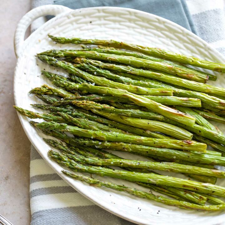 Overhead of cooked asparagus laying on oval white serving platter with tiny side handles.