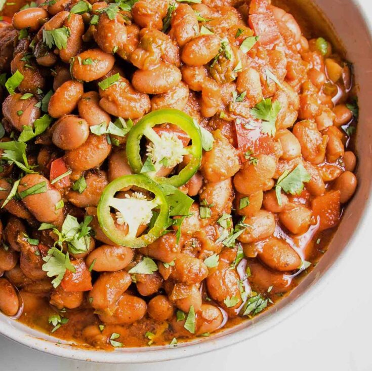 Closeup overhead of baked beans in a bowl, garnished with cilantro and jalapeno slices.