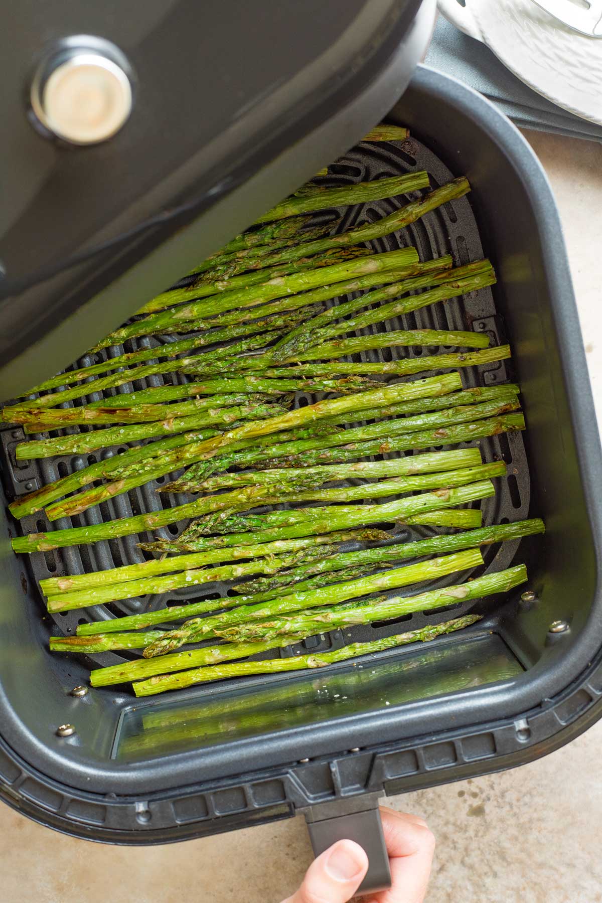 Overhead of hand pulling open air fryer drawer full of cooked asparagus, after cooking is finished.
