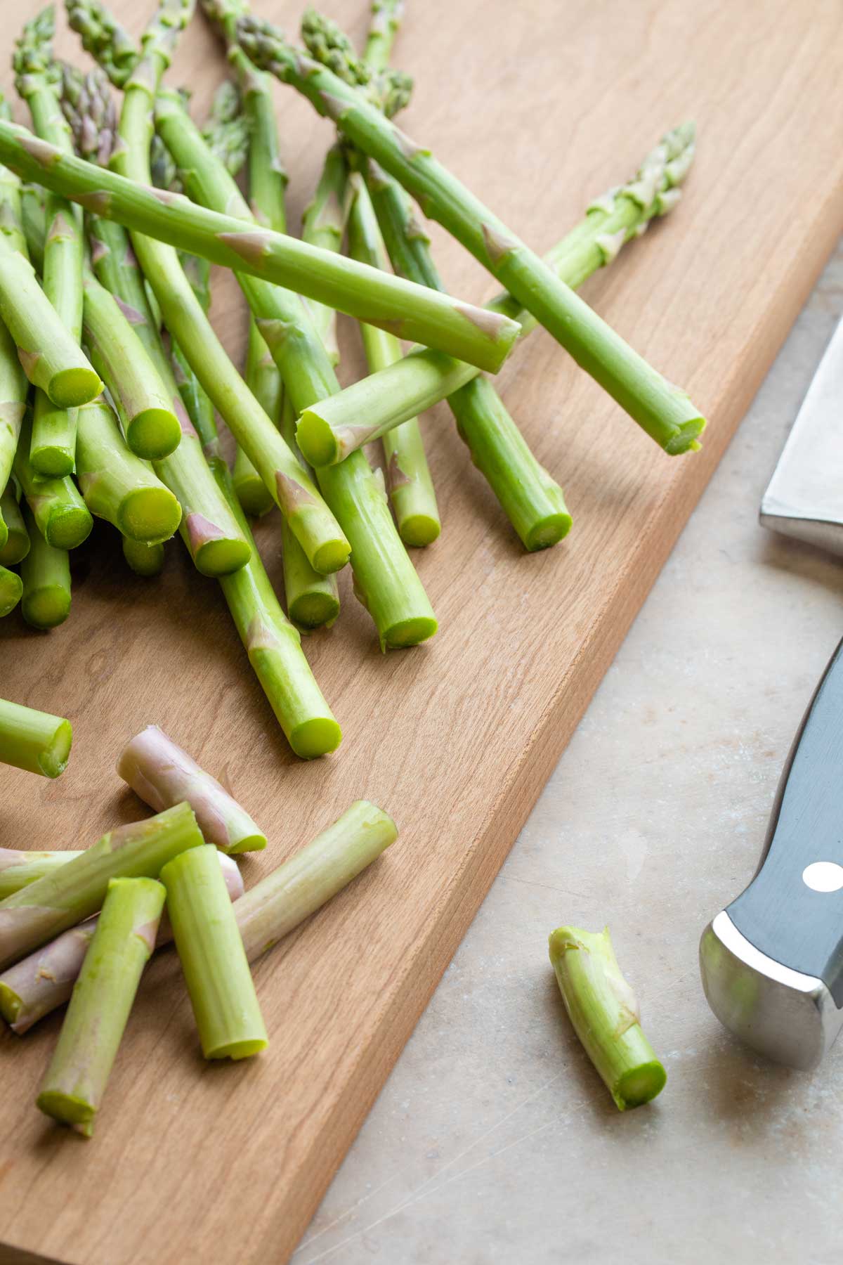 Pile of raw asparagus on cutting board, with ends cut off and knife laying alongside.