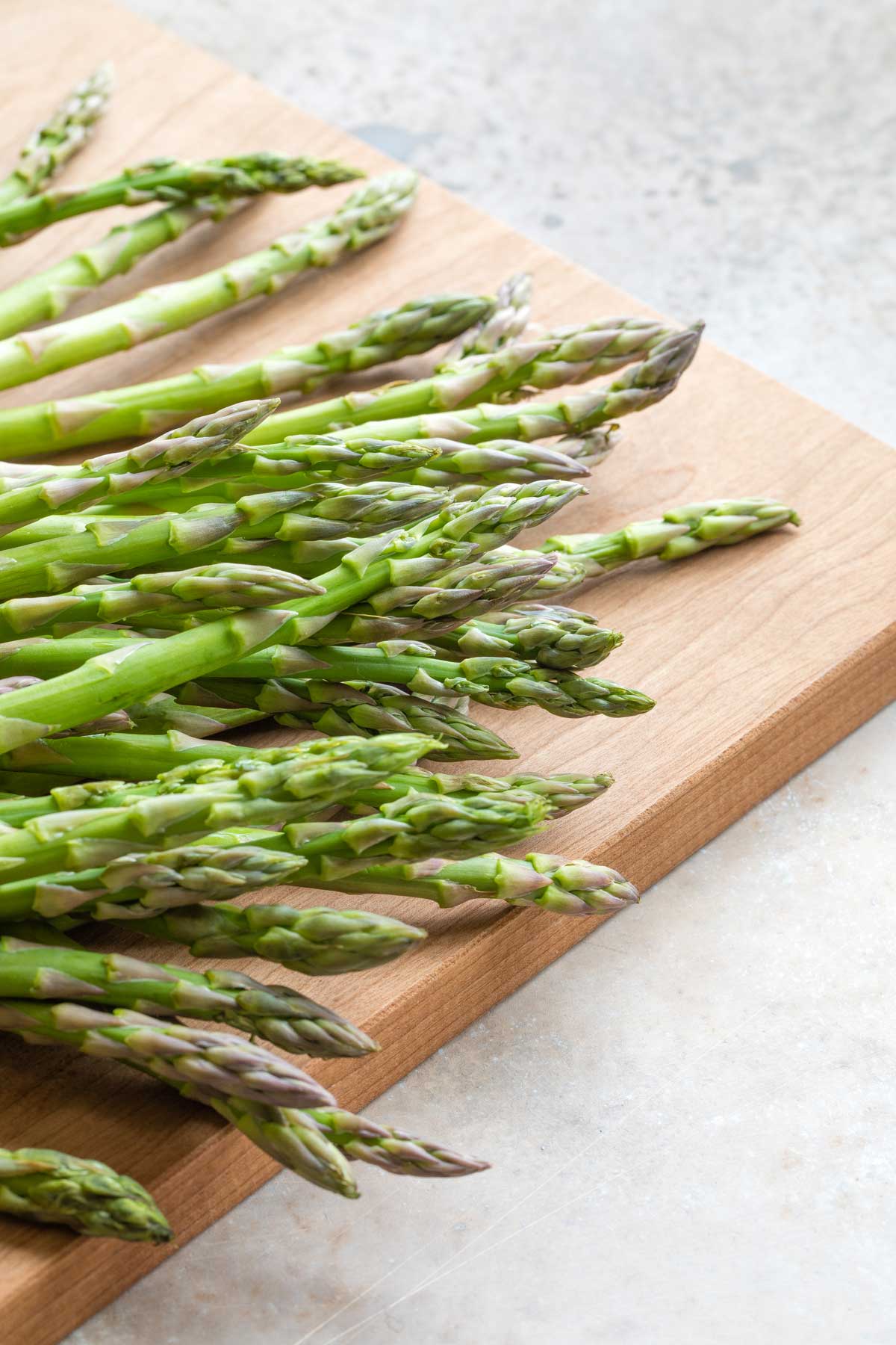 Fresh, raw asparagus laying on wooden cutting board before being prepped for air fryer.