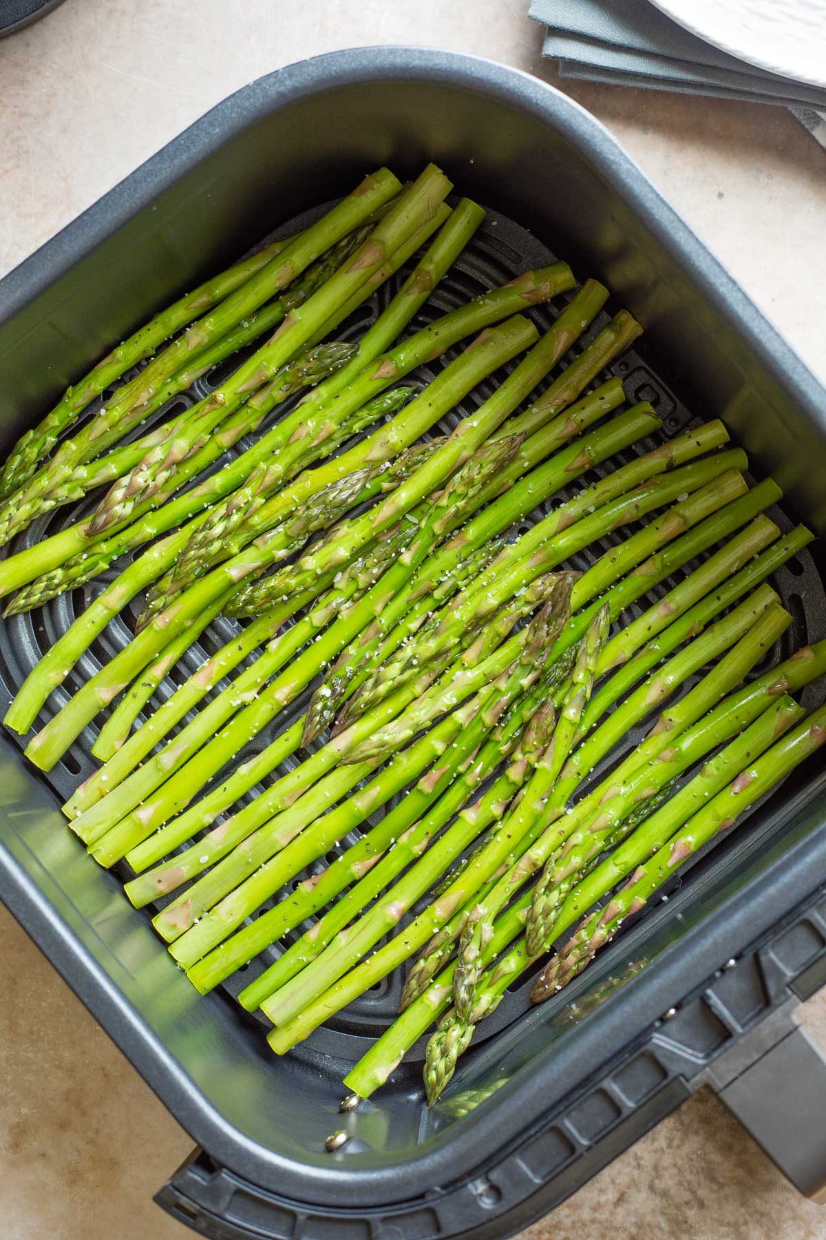 Overhead of raw asparagus spears in single layer in air fryer basket before cooking.