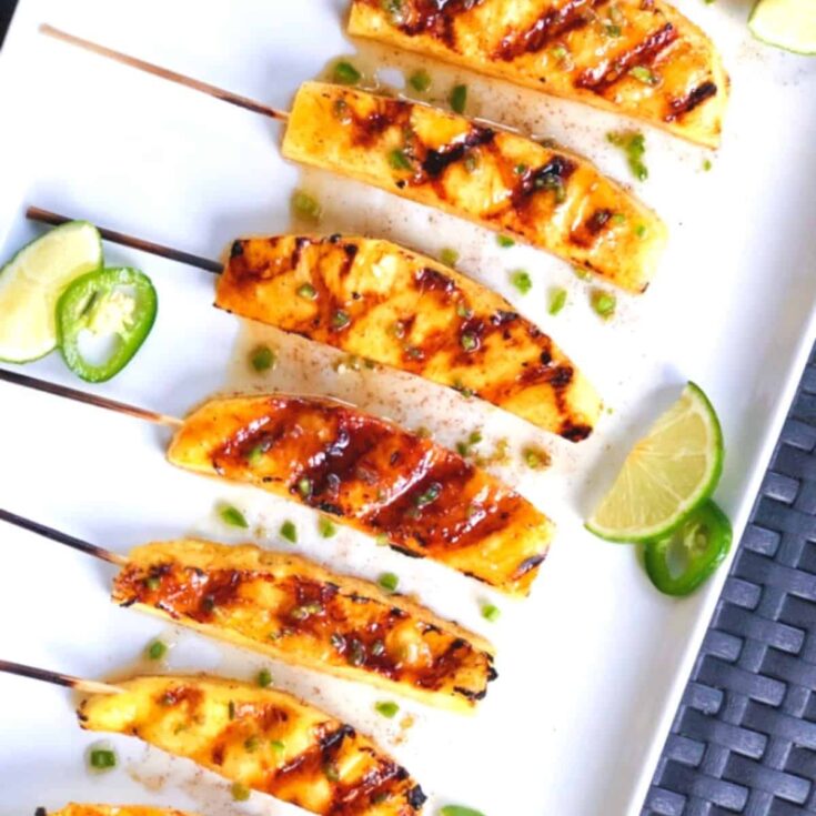 BBQ grilled skewers on shite serving plate with garnish of jalapeno and lime slices on blue-weave cookout placemat.