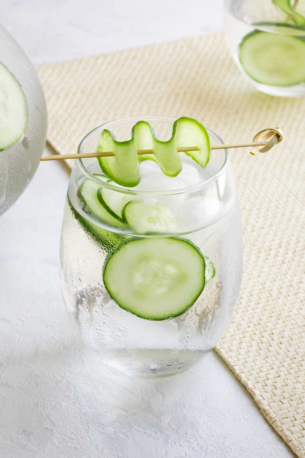 Closeup of one glassful, with a skewered cucumber slice laying decoratively across the top.