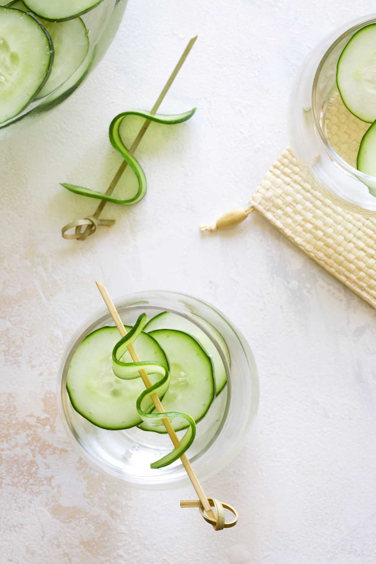 Overhead of a full water glass with a decoratively skewered cucumber squiggle laying across its top.