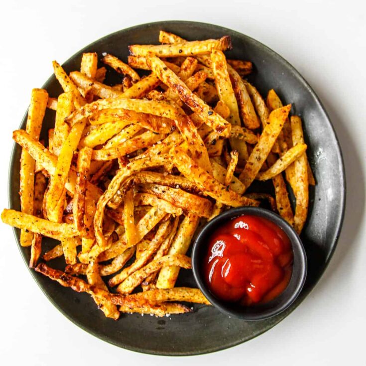 Overhead of the fries on a dark green serving plate with a little side dish full of ketchup.