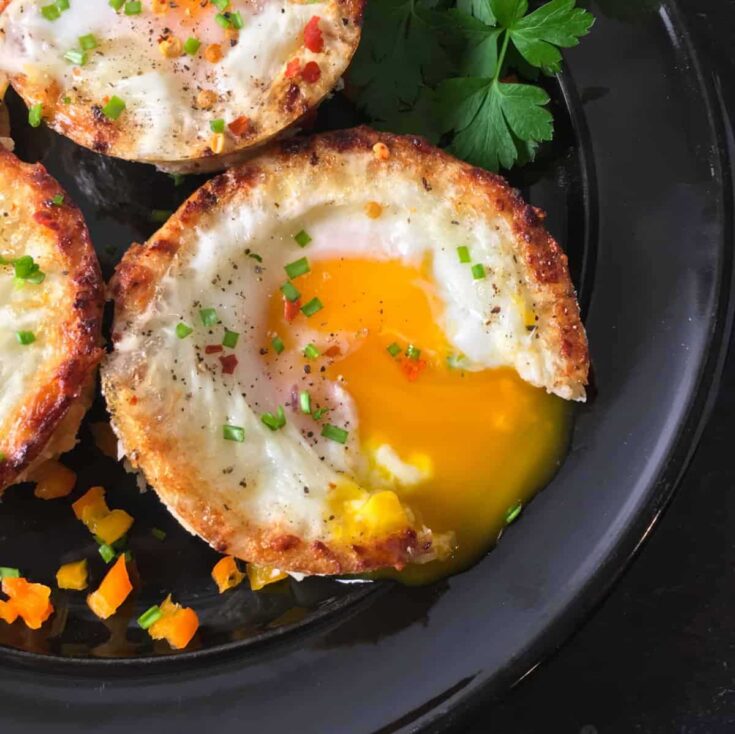 Closeup overhead of one egg cup on black plate with runny yolk oozing out.
