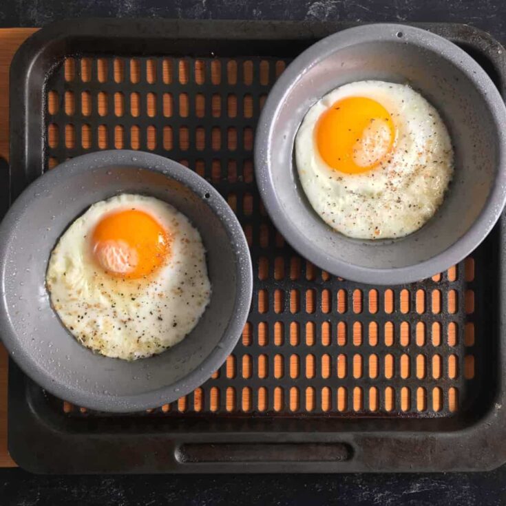 Overhead of two metal dishes with cooked eggs, still in air fryer basket.