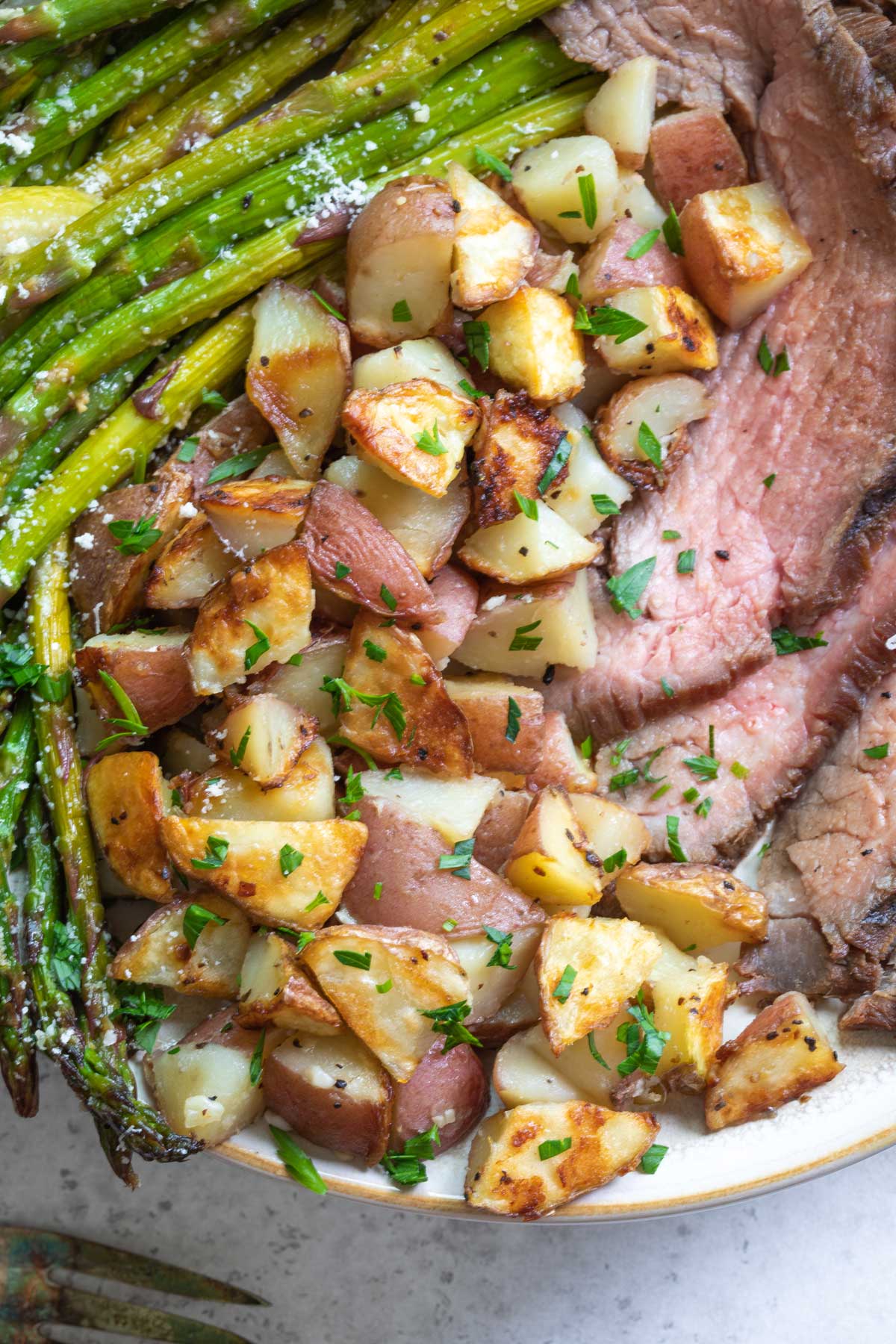 Closeup of potatoes plated between grilled asparagus and sliced flank steak.