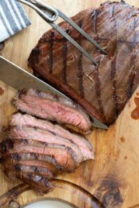 Carving fork holding steak as a long knife makes thin slices.