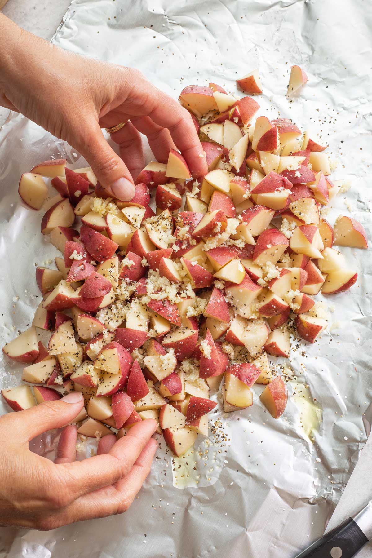 Two hands tossing potatoes with other ingredients before grilling.