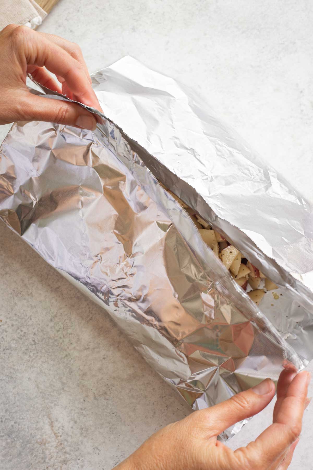 Two hands closing foil over potatoes.