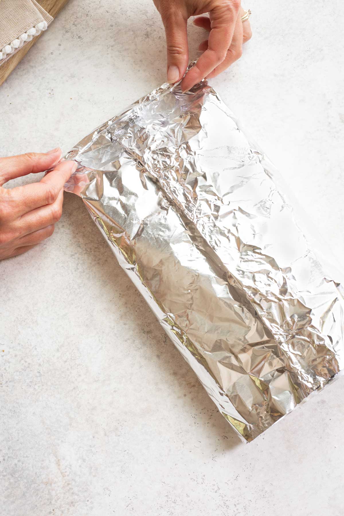 Two hands folding in one end of foil.