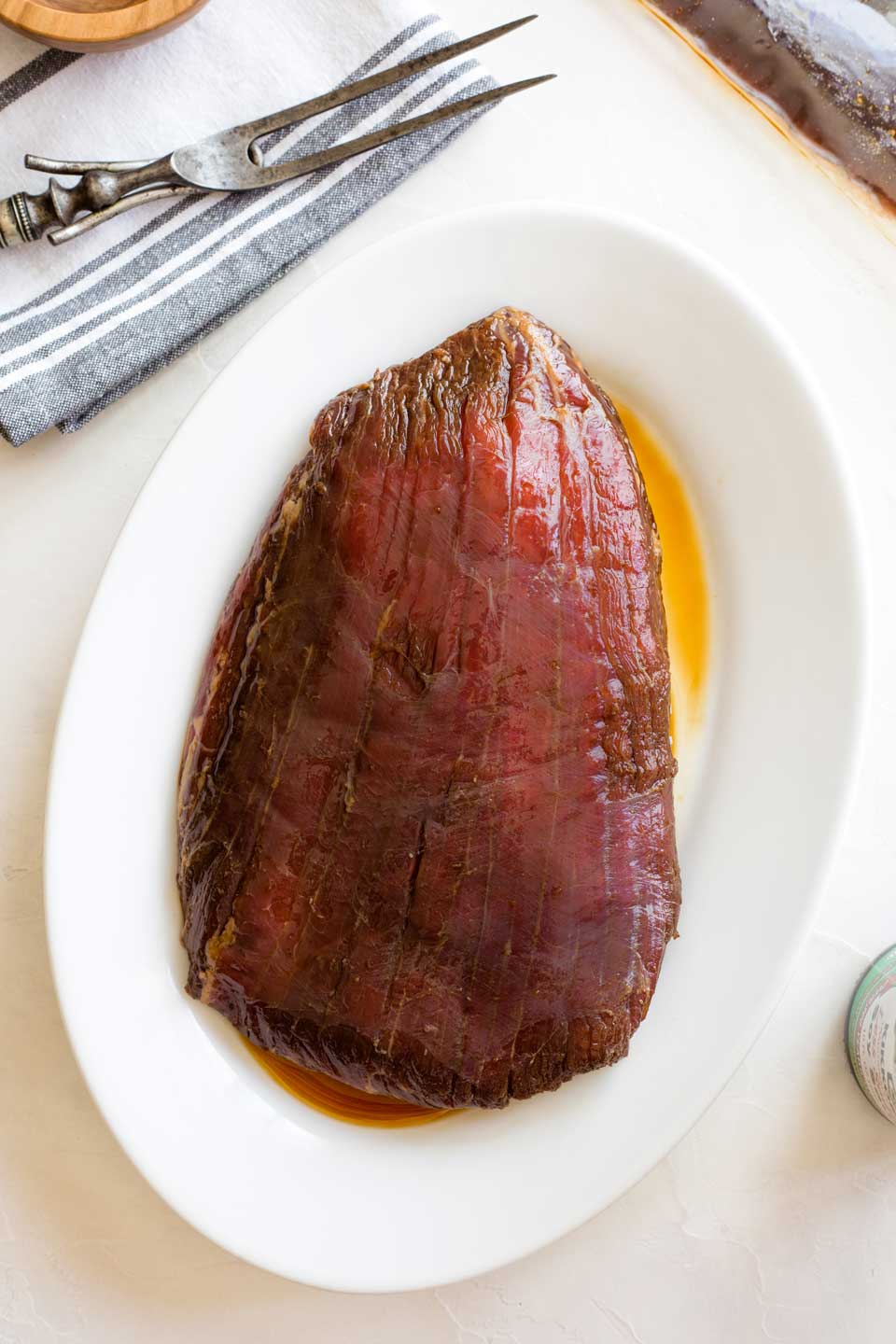 Marinated flank steak on white oval plate before being grilled.