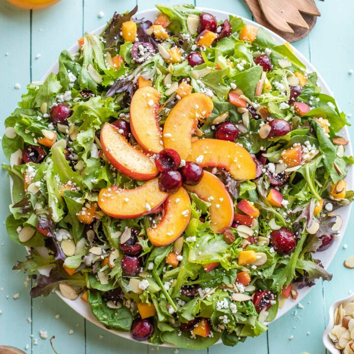 Finished salad on serving platter with sunshine made out of peaches decoratively at center.