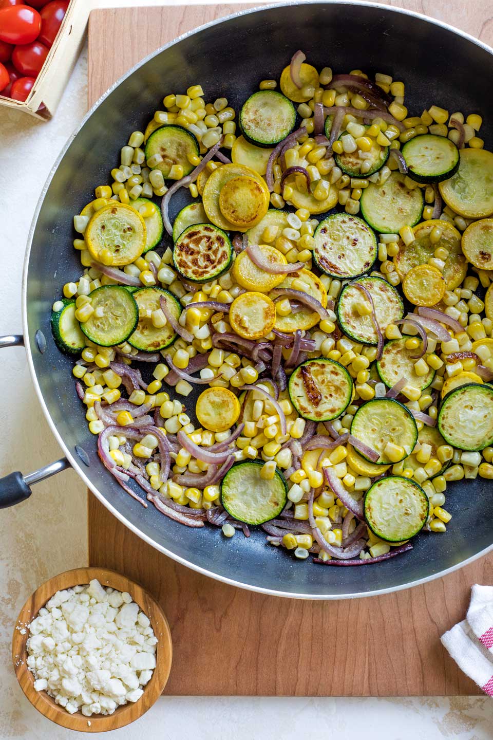 Overhead of zucchini, squash, corn and onions stirred in skillet.