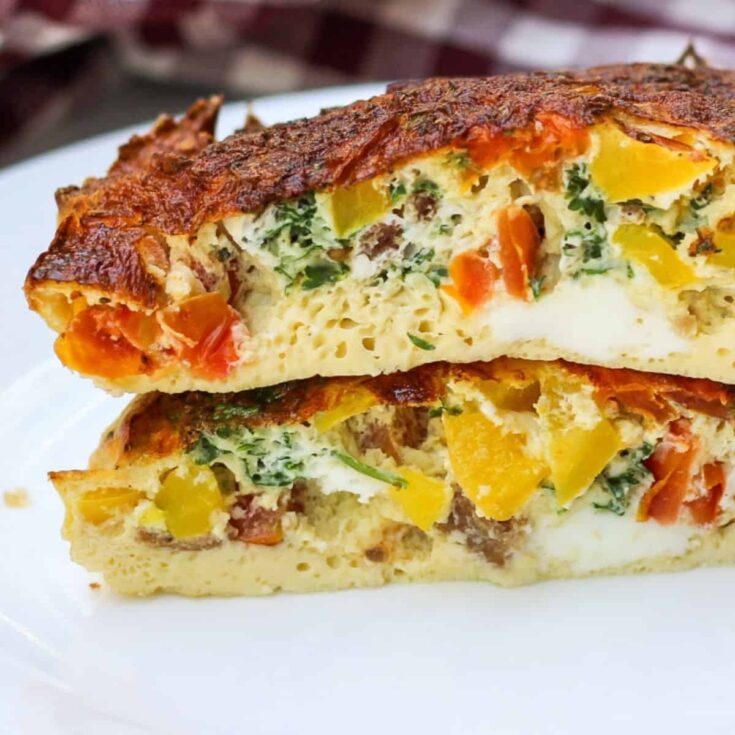 Side view of two cut slices of omelet, stacked on top of each other on a white plate, so you can see the fluffy cooked egg and fillings inside.