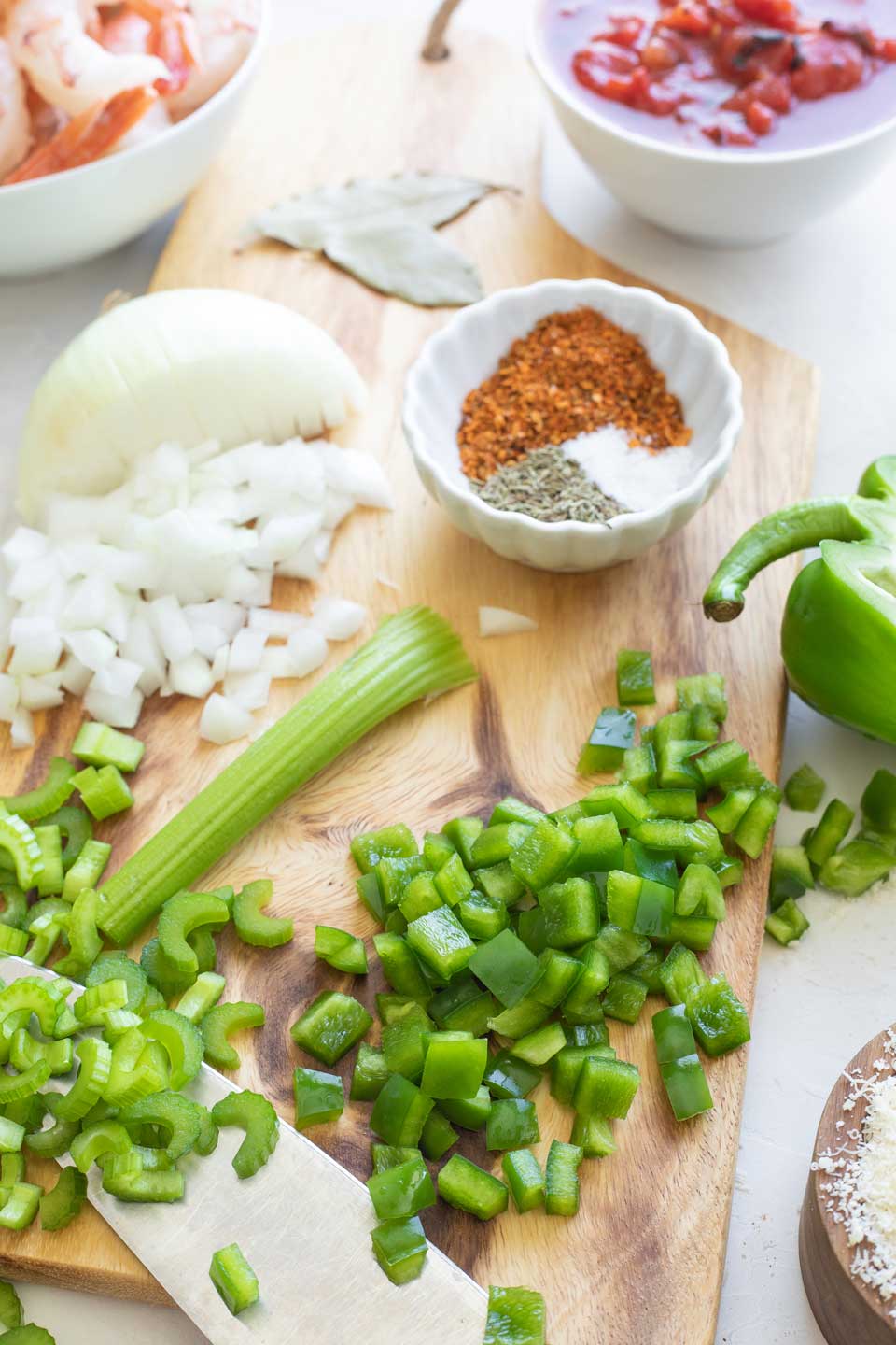 Chopped green peppers, celery and onion on cutting board, surrounded by other ingredients.