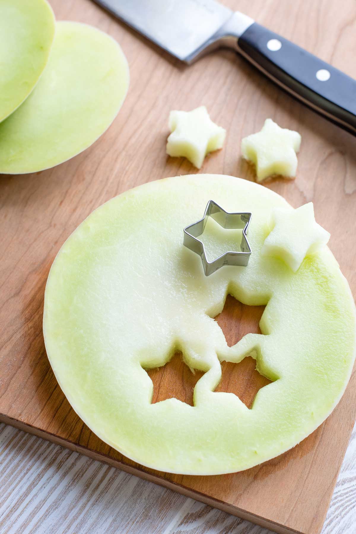 Small cookie cutter cutting stars from a plank of green honeydew melon.