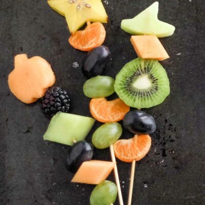 Pinnable image of three fruit kababs with Halloween shapes, on black sheet pan background.
