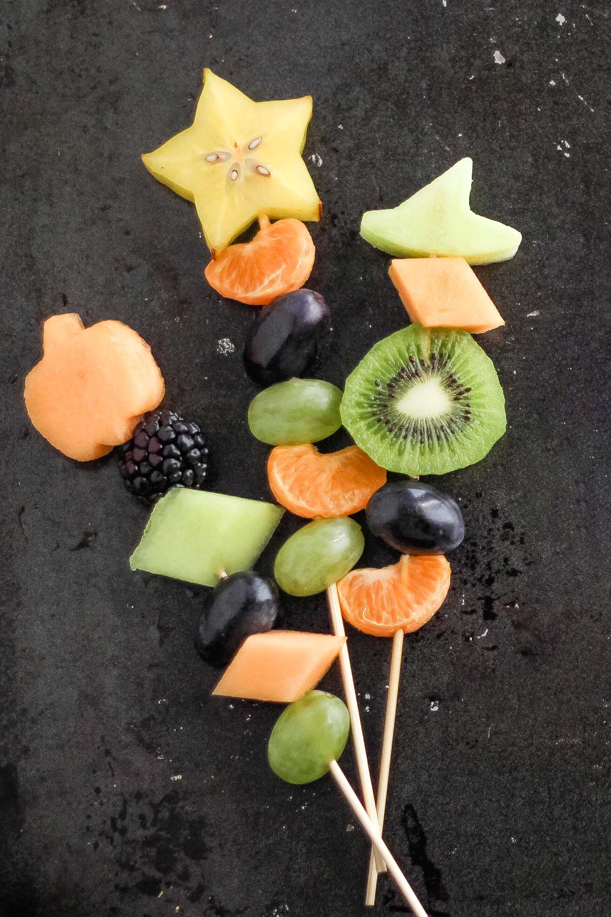 3 skewers with fruit chunks, each topped with a Halloween shape (pumpkin, star and witch's hat).