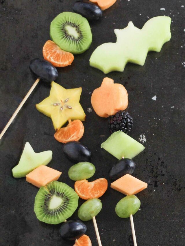 Four kebabs at various angles on black background, with fruit cutout of a bat from a green honeydew melon.