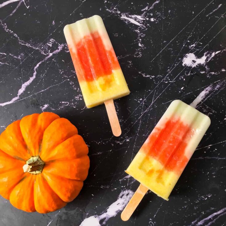 Two fruit pops laying on black surface with decorative mini pumpkin.