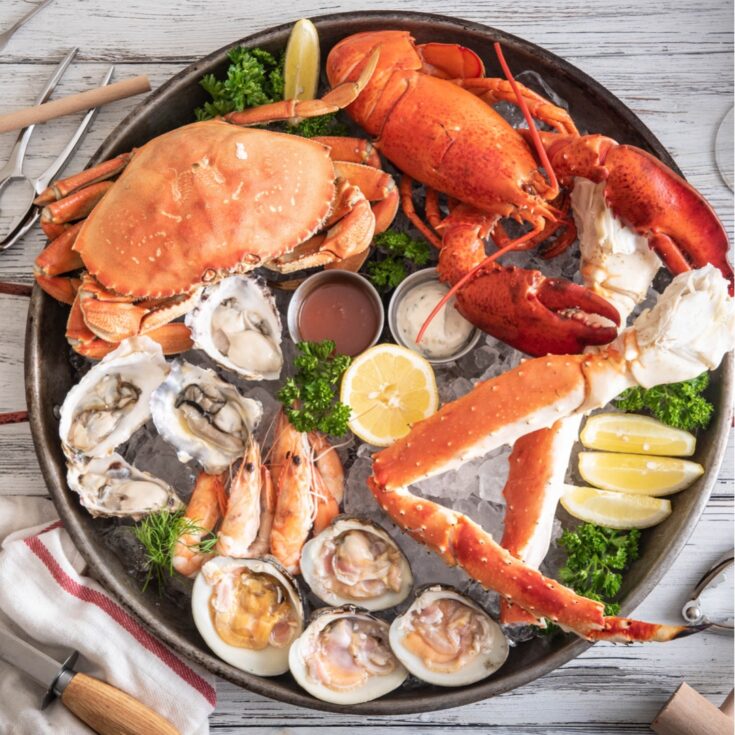 Overhead of Thanksgiving seafood assortment atop ice in a round metal platter, with crab crackers and other implements alongside.