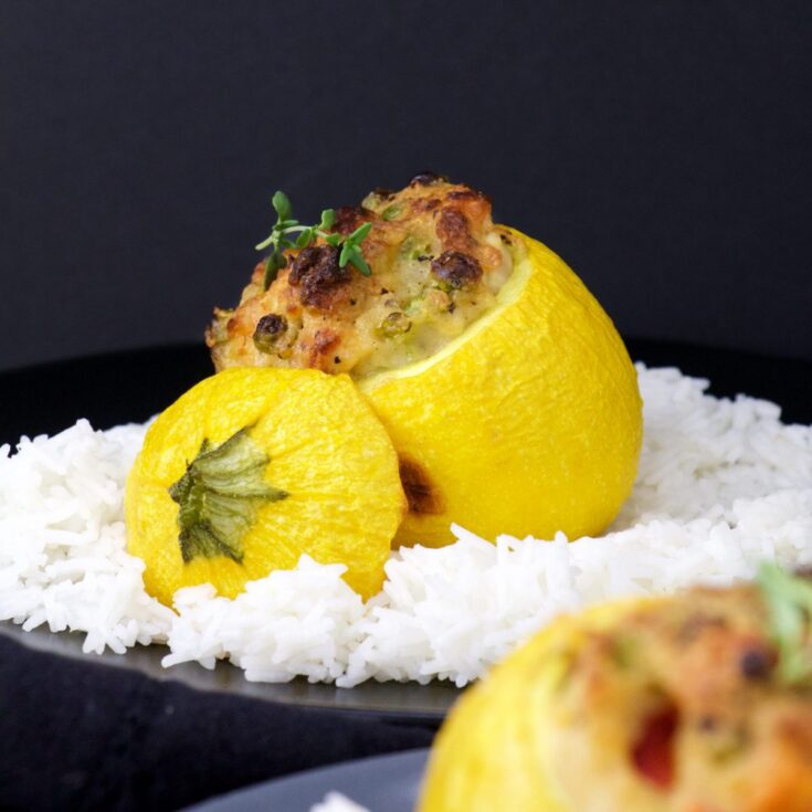 Closeup of one stuffed squash amid white rice on black plate, with another blurry in foreground.