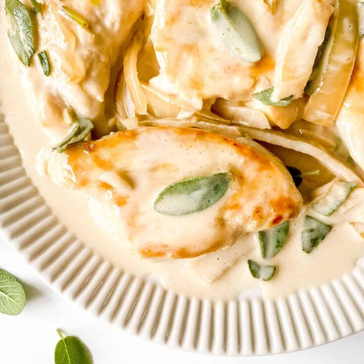 Overhead of cooked chicken on ridged serving plate, garnished with fresh sage.