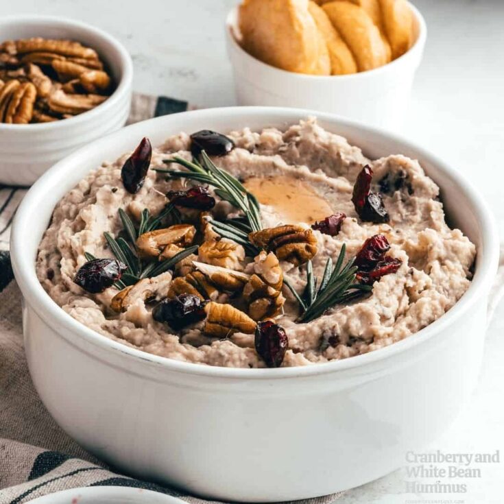 Hummus in white bowl with bowls of extra nuts and crackers behind.