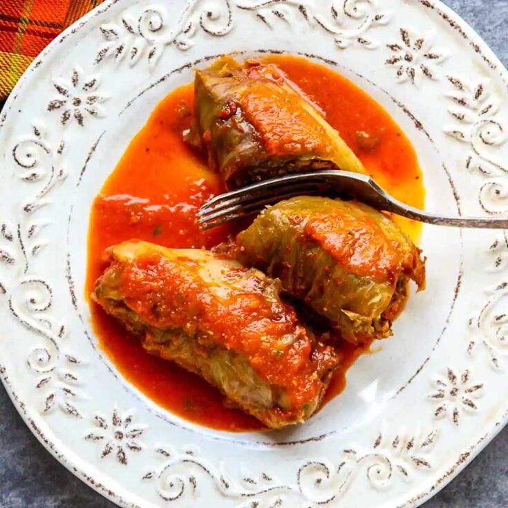 Overhead of two cabbage rolls on decorative white plate with a fork slicing down into one.