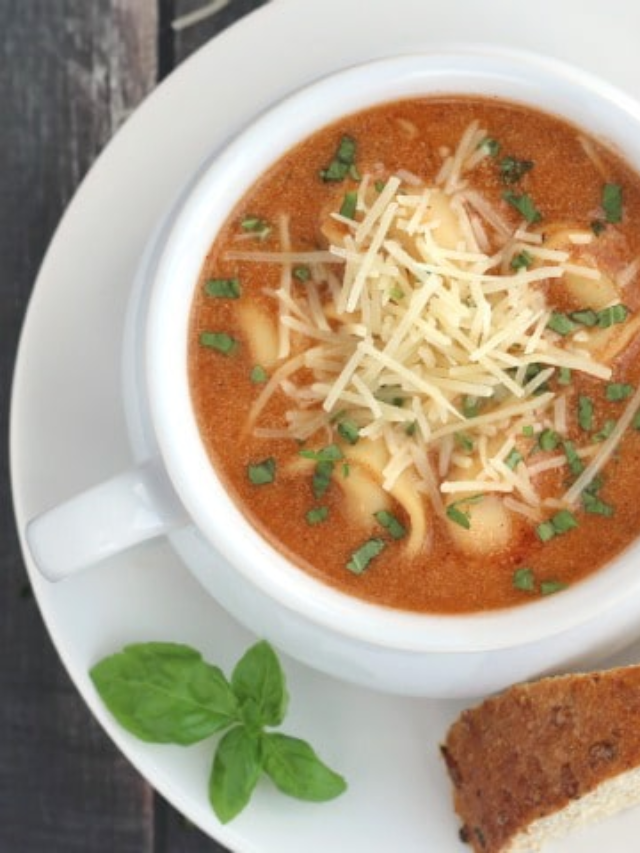 Easy Tomato Basil with Tortellini Recipe Cover image overhead of left side of soup bowl garnished with shredded parmesan and basil.