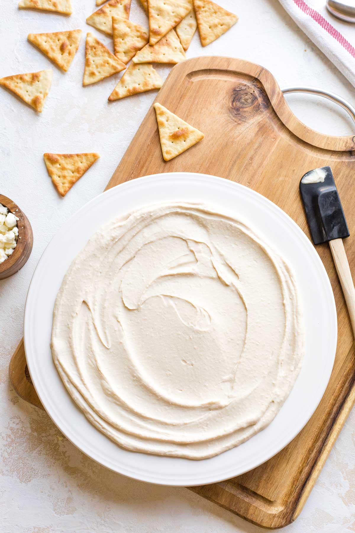 Overhead of cream cheese layer spread on white serving platter on cutting board with crackers scattered nearby.