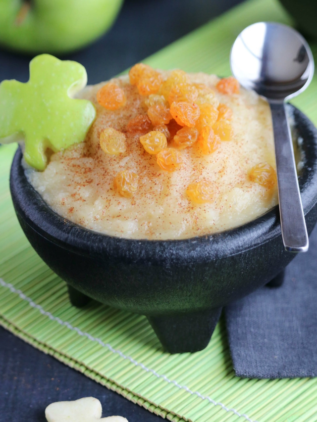 Closuep of one bowl of applesauce with spoon across top and shamrock apple garnish at side.