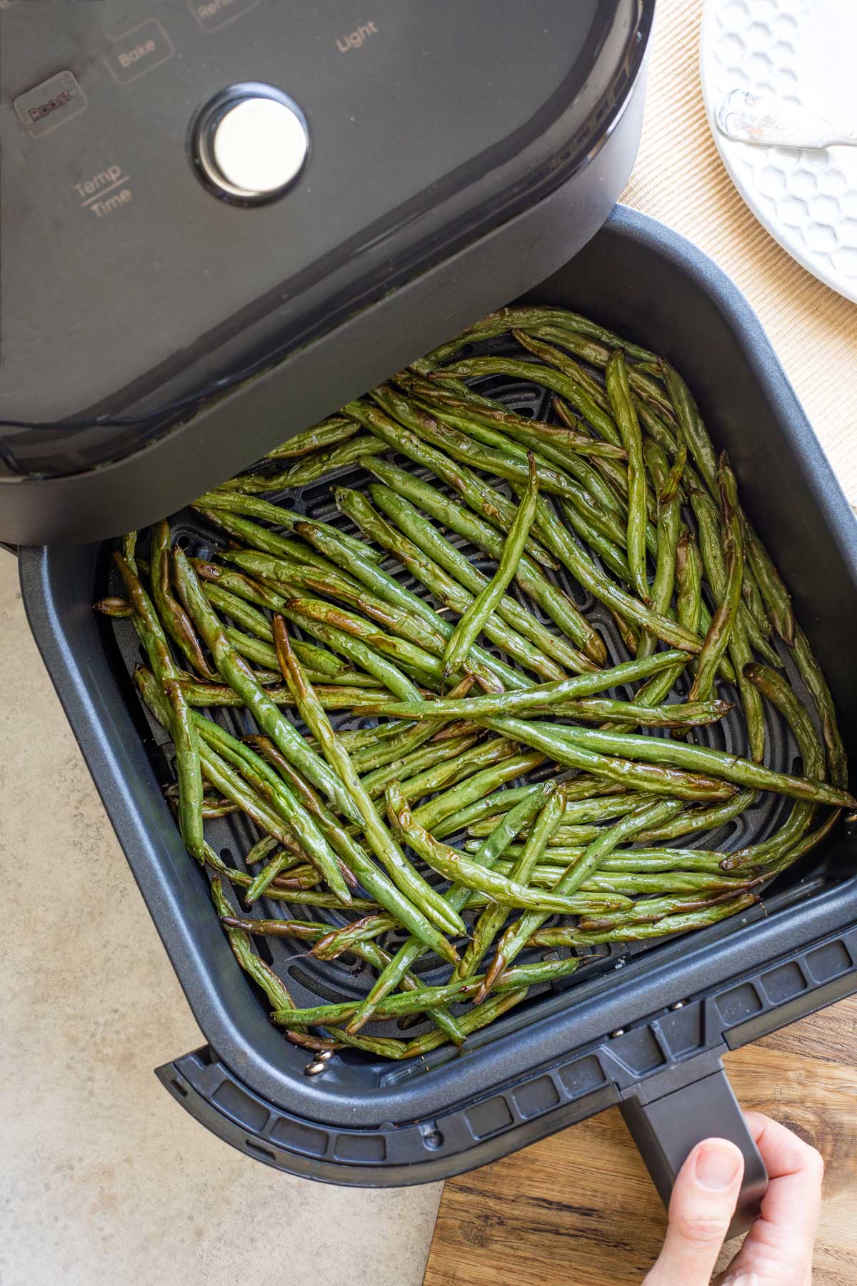 Hand pulling air fryer basket out to reveal cooked green beans.