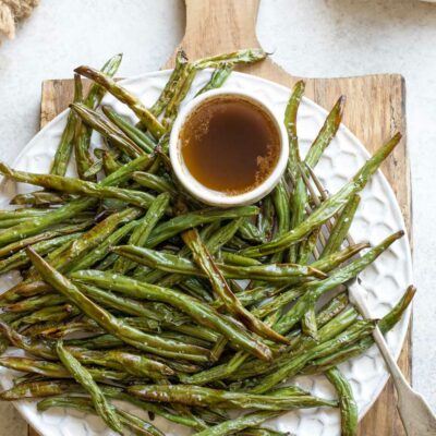 Pinnable image of serving platter of air fried green beans with butter sauce on handled wooden cutting board.