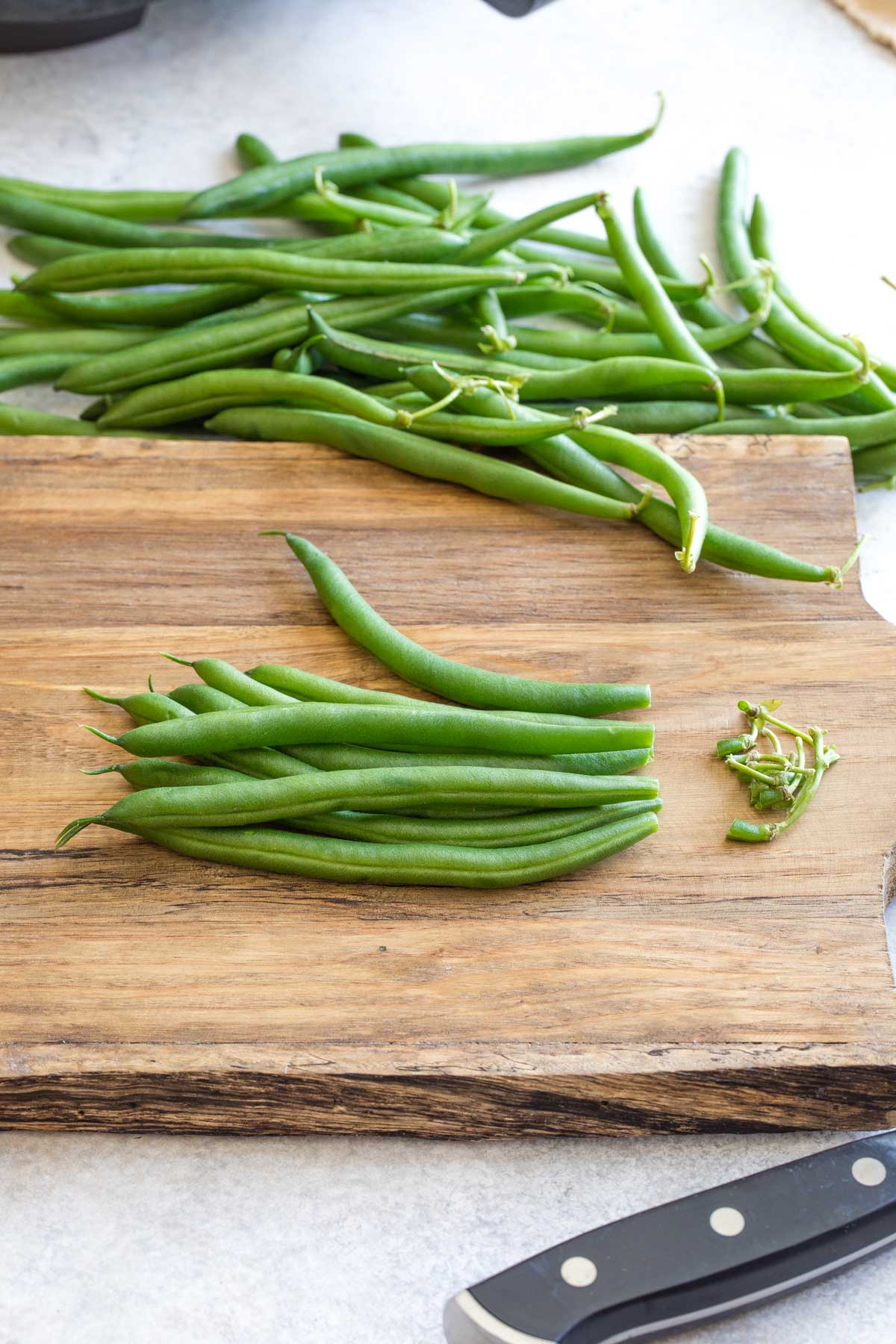 Small pile of green beans gathered together on cutting board to show how to trim off several stems at once.