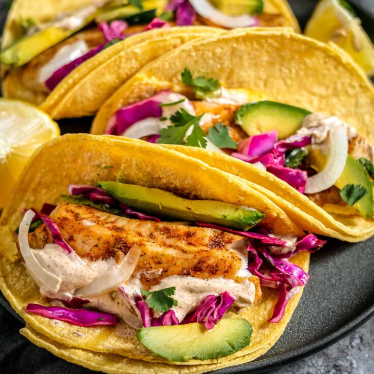 Closeup of one fish taco with with others tucked behind on black plate.