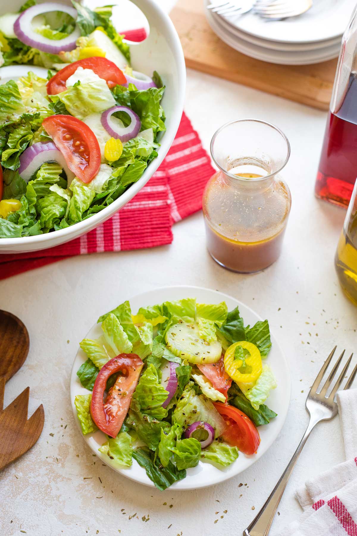 Individual plate of salad, fork, bottle of vinaigrette, serving bowl of salad, extra plates and forks, bottles of oil and red wine vinegar.