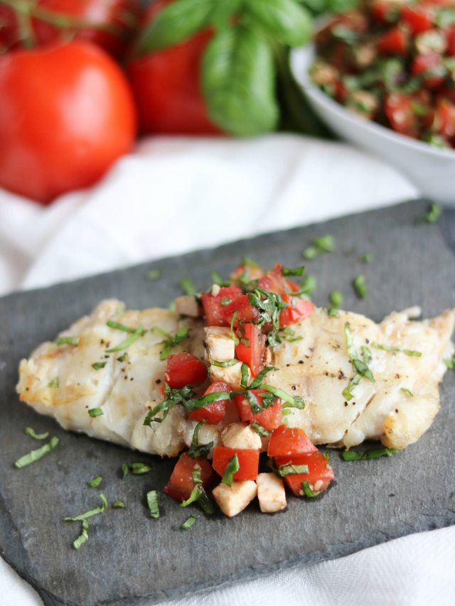 Caprese Grilled Fish Cover image on one portion served on gray slate with extra topping and ingredients in background.