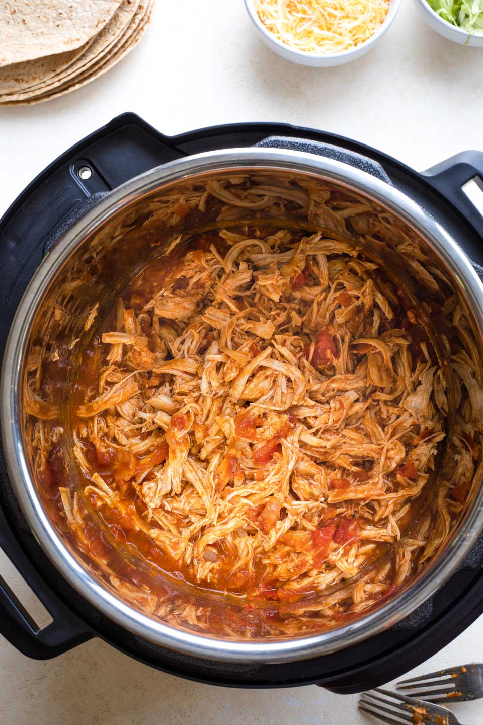 Overhead of cooked and shredded taco chicken still in Instant Pot with taco fixins surrounding.