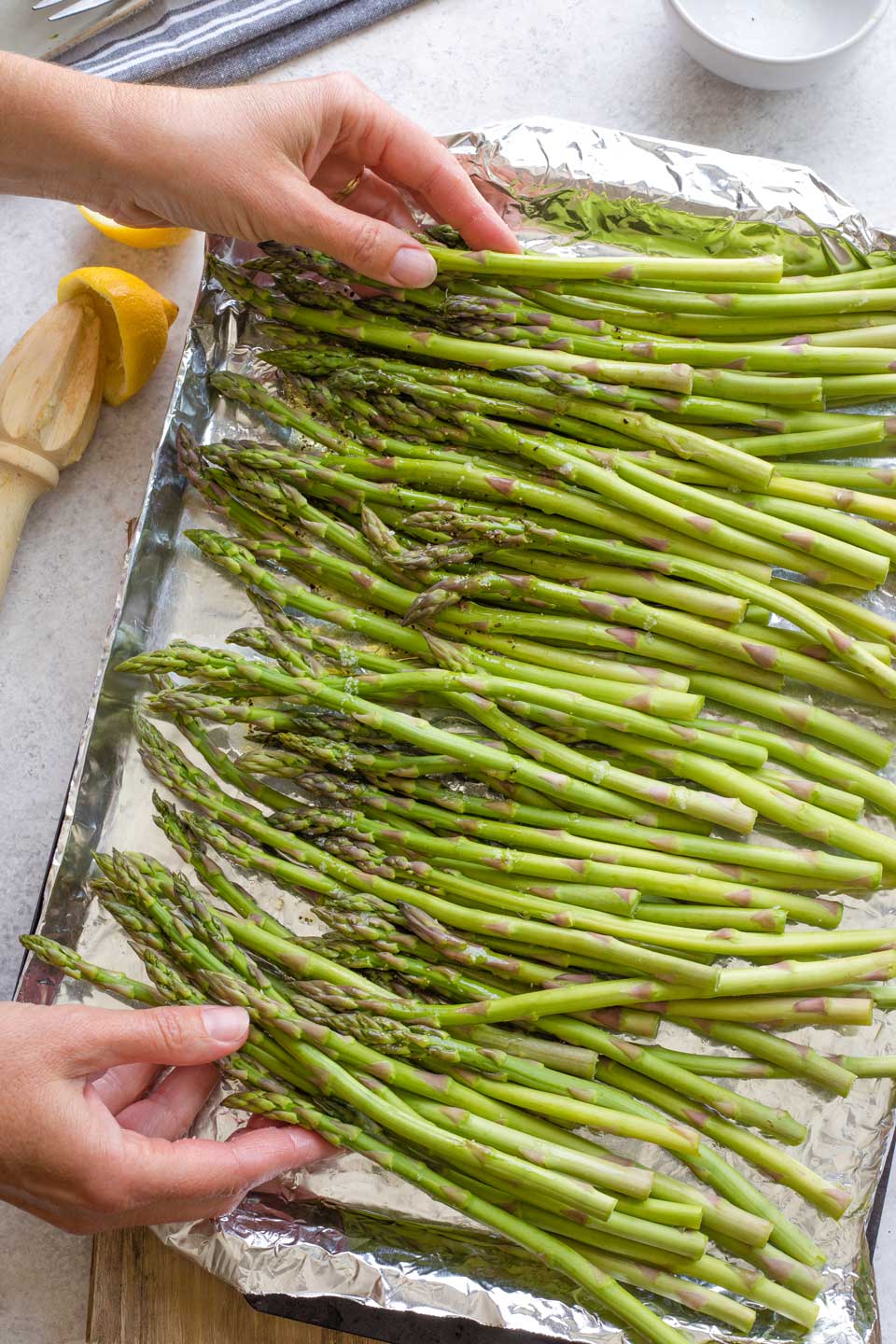 Two hands tossing asparagus in lemon and garlic marinade, on foil-lined grill pan.