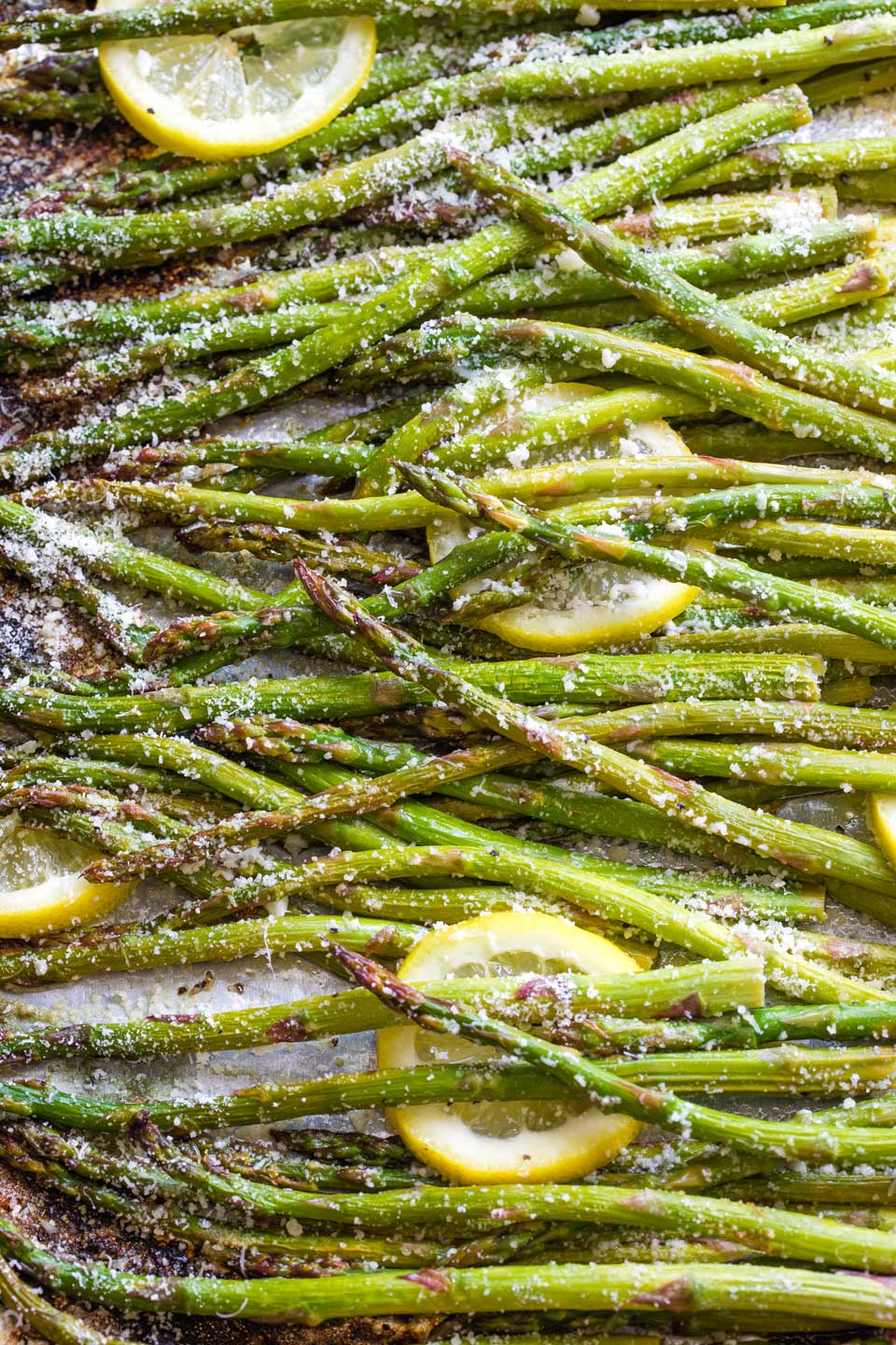 Overhead closeup of asparagus and lemon slices sprinkled with parmesan cheese, still on pan after grilling.