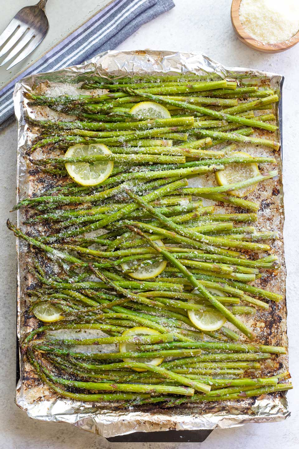 Asparagus still on grill pan, sprinkled with parmesan cheese and with lemon slices tucked in.