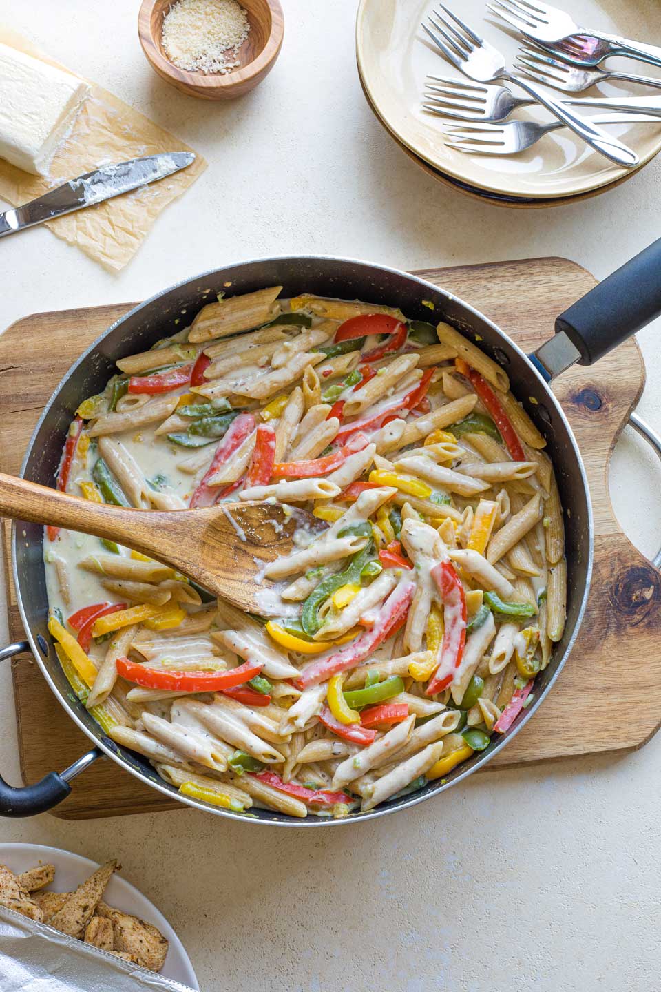 Overhead of wooden spoon stirring creamy pasta in pot before re-adding jerk chicken.