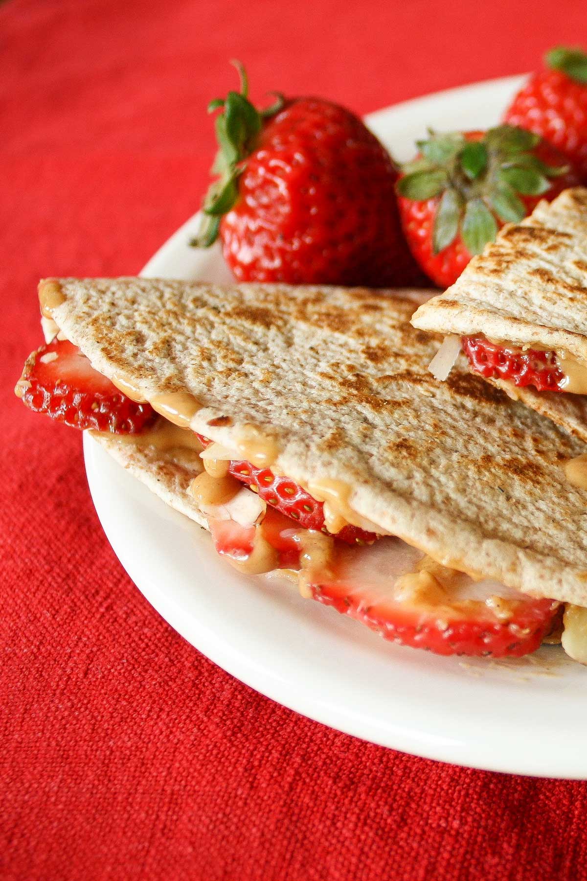 Closeup of on folded, grilled tortilla stuffed with strawberries and warmed peanut butter, garnished with more berries.